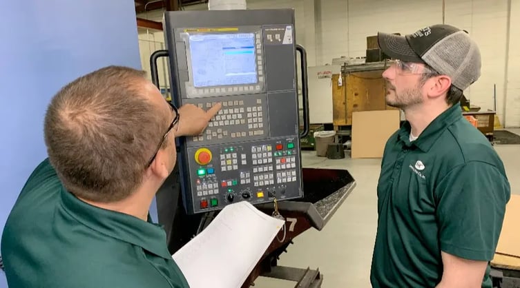 Two workers using G-code to program a CNC machine